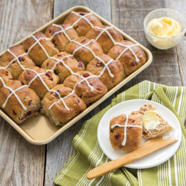 Golden baked breakfast buns in Nordic Ware nonstick quarter sheet pan, one served on white plate with butter