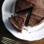 round chocolate cake with chocolate frosting, cake slice cut out of cake, on plate