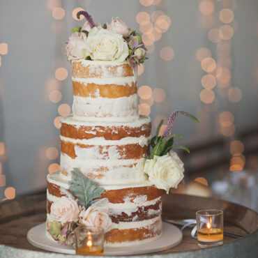 Tiered wedding cake on stand, flowers on top with candles