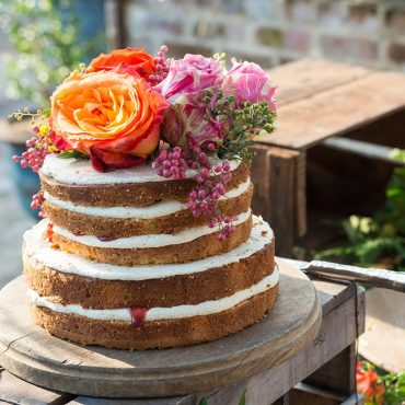 multi tiered cake with white frosting between tiers, variety of flowers on top of cake