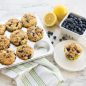 baked blueberry muffins in pan, one muffin on plate, fresh blueberries an lemons on counter