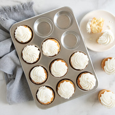 Cupcakes with white frosting in muffin pan, one on plate