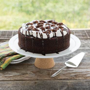Chocolate layer cake with white frosting and chocolate drizzle on cake stand, baked in Nordic Ware round pan