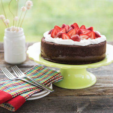 Chocolate cake with whipped cream and sliced strawberries on green cake stand, baked in Nordic Ware round pan