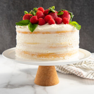Nordic Ware round cake pan with glazed vanilla layer cake topped with fresh raspberries and mint on stand
