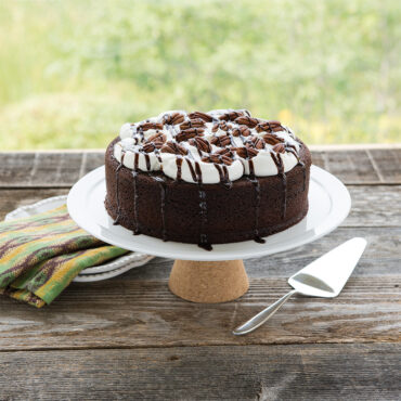 Chocolate layer cake with whipped cream and pecans on wooden cake stand, Nordic Ware cake server nearby