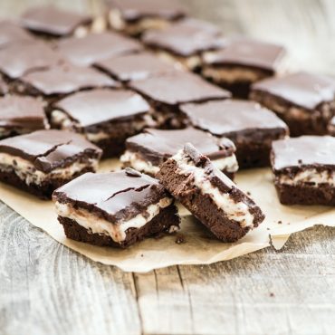 Chocolate layer bars with vanilla filling and chocolate frosting on parchment paper