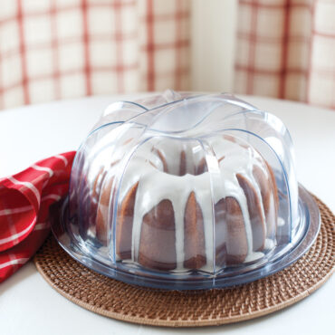 Glazed bundt cake displayed in clear Nordic Ware plastic cake keeper with domed lid and handles