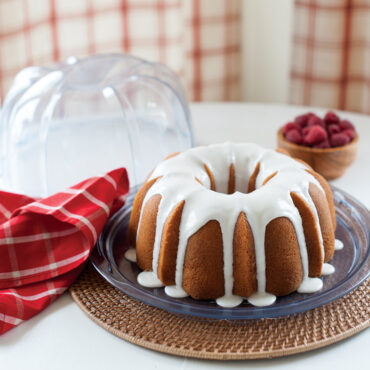 Glazed bundt cake in Nordic Ware clear plastic cake keeper with domed lid opened, showing golden cake
