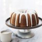 Glazed baked Bundt on a silver cake stand, glaze container on surface