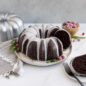 Chocolate Baked Bundt cake cut into with a white glaze and cranberries in background.