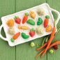 Glazed veggie cakelets on basket design platter, fresh vegetables such as carrots, pea pods and radishes on green wooden surface.