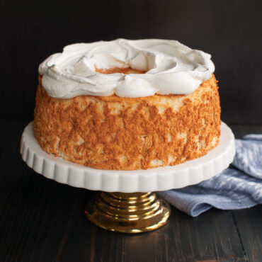 Golden angel food cake with whipped cream on white pedestal cake stand