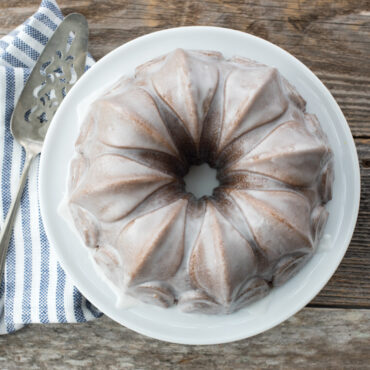 Golden bundt cake with white glaze baked in Nordic Ware Fleur-de-Lis pan, showing fluted petal design