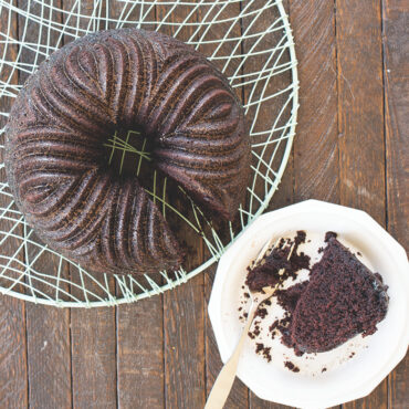 Dark chocolate bundt cake with intricate fluted design on cooling rack, single slice plated showing moist interior