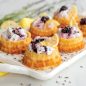 Baked basket cakes filled with whipped cream and blackberries, lemon slice garnish, on tray