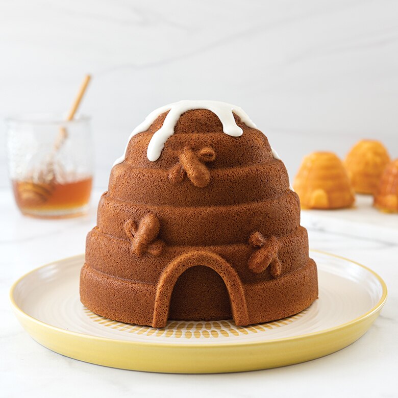 baked beehive cake with white glaze, beehive cakelets in background with honey