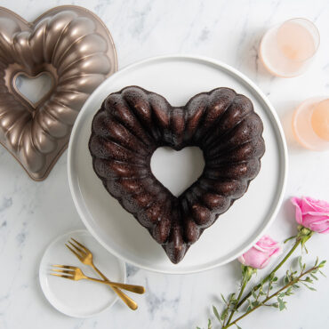 Plain Elegant Heart Bundt cake on white cake stand, surrounded by pink roses and pan, overhead