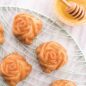 Baked rose cakes with honey glaze, on cooling rack, honey in bowl with dipper