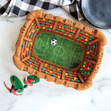 Soccer theme Stadium Bundt Cake with plates, towel, and soccer figurines on the side.