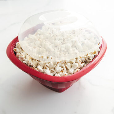 Nordic Ware red Pro Pop Popper bowl filled with freshly popped white and yellow popcorn kernels
