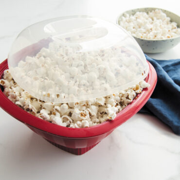 Nordic Ware red Pro Pop Popper bowl filled with freshly popped white and yellow popcorn kernels