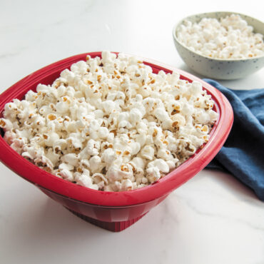 Nordic Ware red Pro Pop Popper bowl filled with freshly popped white and yellow popcorn kernels
