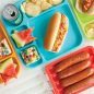 Microwaved brats in open steamer, picnic plate with brat, condiments in bun, watermelon wedges, rice krispy bar, chips