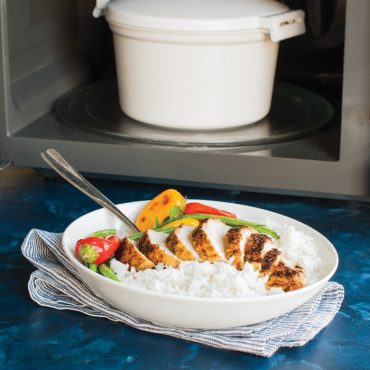 Wide bowl with sliced chicken, vegetables, and cooked rice; rice cooker in open microwave