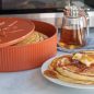 Warmer with cooked pancakes, pancakes on plate with syrup and butter, syrup container
