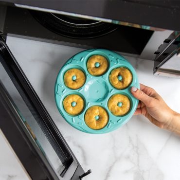 Donut Bites Pan filled with batter, hand putting into open microwave.