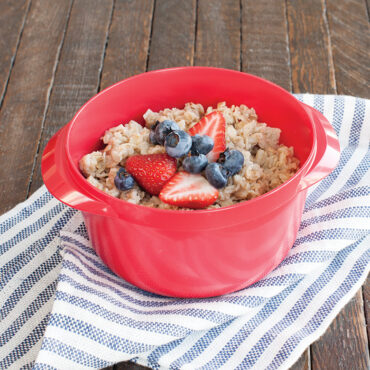 White ceramic Nordic Ware Multi Boiler bowl with cooked oatmeal topped with fresh strawberry slices and blueberries