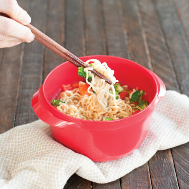 Nordic Ware multi-boiler pot with cooked ramen noodles, broth, and vegetables, wooden chopsticks resting on rim