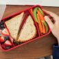 Bento Box container compartments with fresh fruit, sandwich, carrots and snap peas on desk