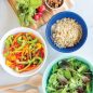 3 bowls with salad ingredients, wooden spoon, vegetables on cutting board