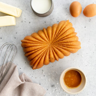 Baked salted caramel loaf in Fluted loaf design surrounded by ingredients  needed with mix