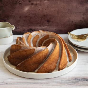 Golden bundt cake with white glaze drizzle baked in Nordic Ware Heritage bundt pan, showing spiral fluted design