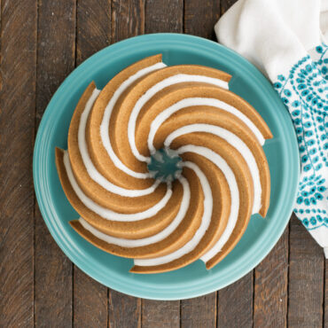 Golden bundt cake with white glaze drizzle baked in Nordic Ware Heritage bundt pan, showing spiral fluted design