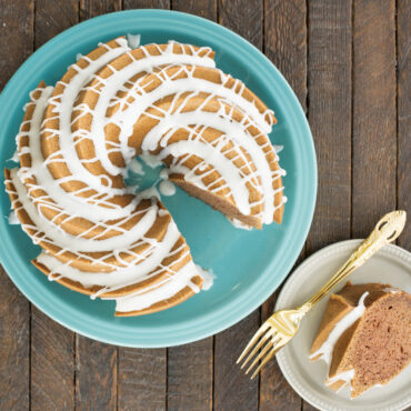 Sliced bundt cake with white glaze drizzle on turquoise plate, showing Nordic Ware Heritage pan's detailed fluted pattern