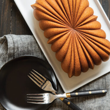 Golden fluted loaf cake on white serving plate with two silver forks, showing detailed ridged pattern from Nordic Ware pan