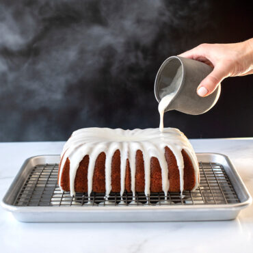 Golden fluted loaf cake from Nordic Ware Classic Fluted Loaf Pan being drizzled with white vanilla glaze