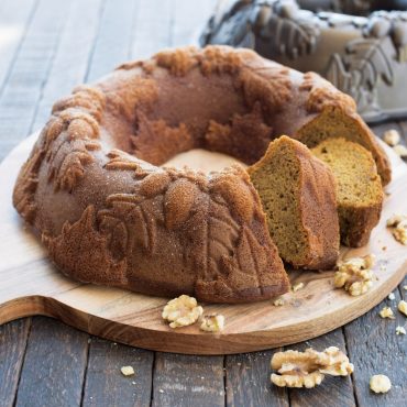 Baked spice wreath cake dusted with powdered sugar on wood serving plate, two slices cut from cake