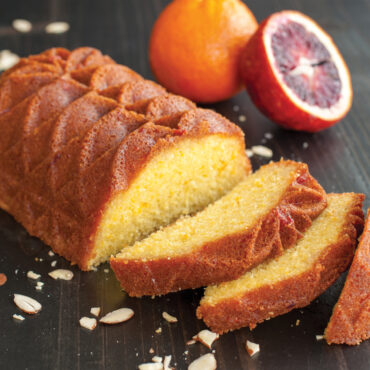 Golden blood orange loaf cake baked in Nordic Ware Jubilee pan, sliced to show moist interior, oranges nearby