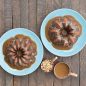 Top view baked spice duet Bundt cakes with caramel glaze on plates, caramel glaze in cup, chopped nuts in cup