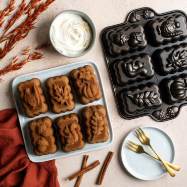 Harvest Mini Loaf Cakes on plate next to pan with dish of whipped cream and cinnamon sticks in scene