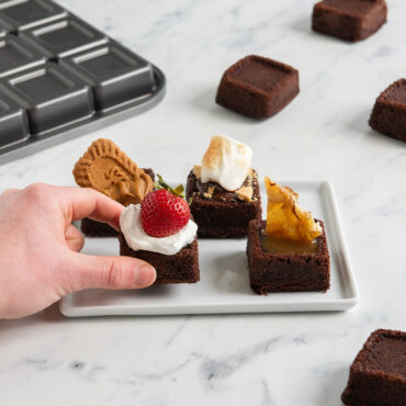 hand grabbing brown brownie bites baked in Nordic Ware pan with various toppings