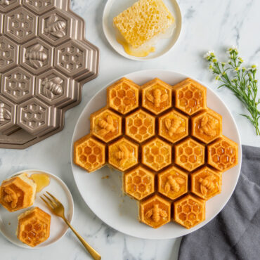 Golden honeycomb pull-apart cake covered with honey with some pieces cut out and plated and pan with small plate of honey comb drizzled with honey