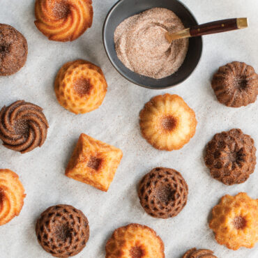 sugared bundt charm tea cakes spread out on parchment paper with bowl of brown sugar