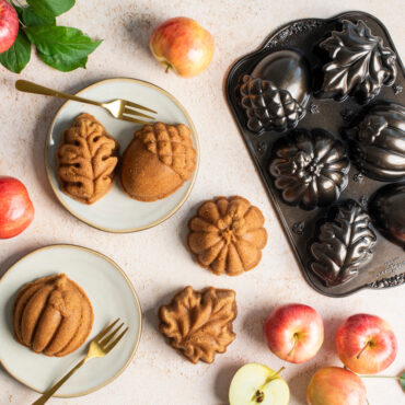 Small cakes baked in Nordic Ware Autumn Treats pan on small plates surrounded by apples