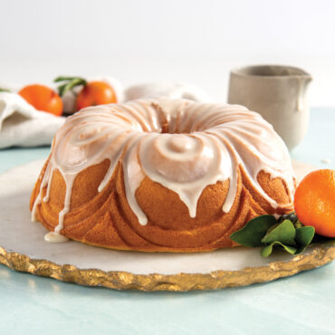 Golden bundt cake with white glaze dripping down fluted sides, garnished with fresh citrus and mint leaves